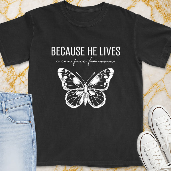 Black t-shirt with white text "BECAUSE HE LIVES i can face tomorrow" and butterfly graphic.