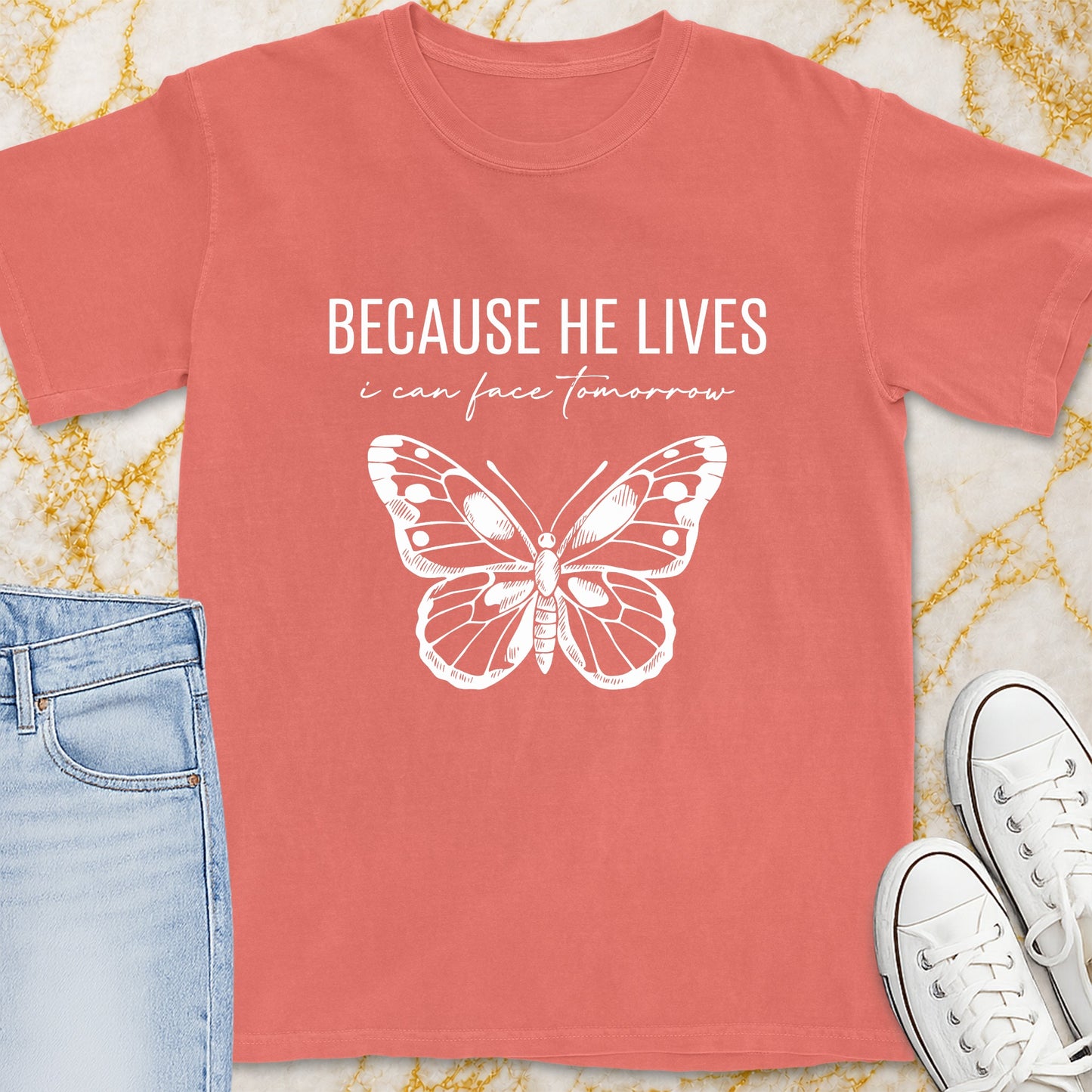 Coral t-shirt with white text "BECAUSE HE LIVES i can face tomorrow" and butterfly graphic.