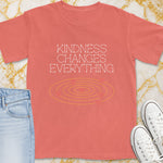 Coral t-shirt with "Kindness Changes Everything" text and heart graphic.